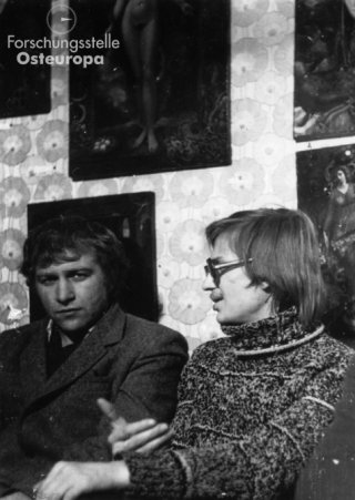 Художественная выставка в квартире Юлии Вознесенской. / Kunstausstellung in der Wohnung von Julia Wosnessenskaja.
Двое неизвестных в квартире Юлии Вознесенской и Владимира Окулова, на стене: художественные работы, 1970-е гг. / Zwei Unbekannte sitzen in Julia Wosnessenskajas und Wladimir Okulows Wohnung, an der Wand hinter ihnen hängen Kunstwerke, 1970er-Jahre.